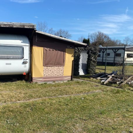 Campingplatz Räumung nähe Ulm Ein Wohnwagen steht neben einem kleinen Holzhaus auf einer grünen Wiese.
